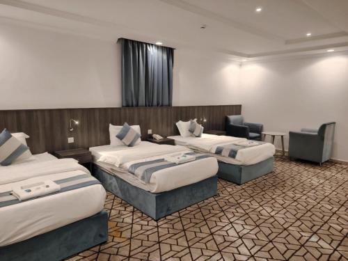 une chambre d'hôtel avec trois lits et une chaise dans l'établissement فندق الأولين حياة - مكه, à Ash Shishah