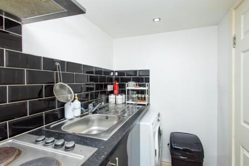 Il comprend une cuisine avec un évier et des murs carrelés noirs. dans l'établissement Cozy Studio Flat, 7mins from CENTRE, Parking, WiFi & Netflix, à Killingbeck