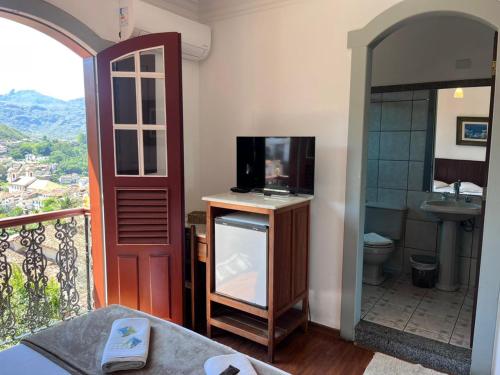 a room with a balcony with a television and a bathroom at Pousada Casa dos Contos in Ouro Preto