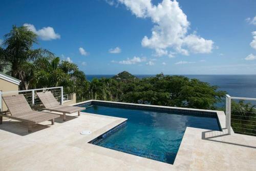 a swimming pool with two chairs and the ocean at Maria Bluff Cottage Villa-Romantic Ocean Views Modern Private Pool in Contant