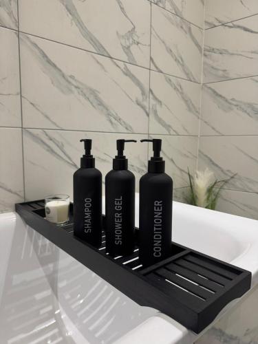 two black shampoo bottles on a shelf next to a bath tub at La Rose Serenity Residence Elegant Rooms in London