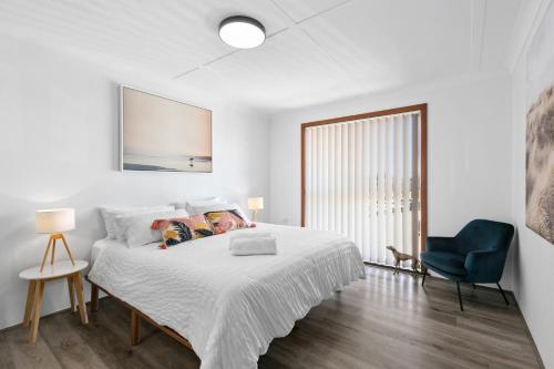 ein weißes Schlafzimmer mit einem Bett und einem blauen Stuhl in der Unterkunft Beachside Nook at Warilla in Lake Illawarra