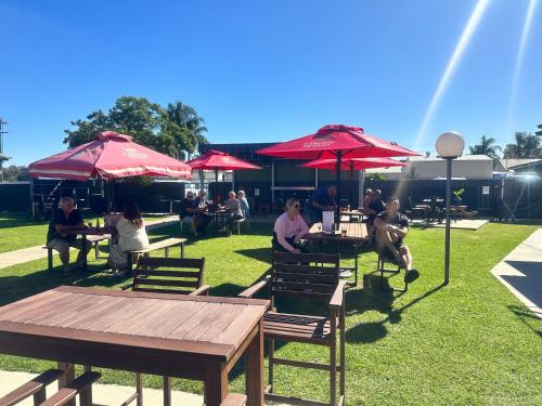 Un grupo de personas sentadas en mesas bajo sombrillas rojas. en Royal Mail Hotel Mulwala, en Mulwala
