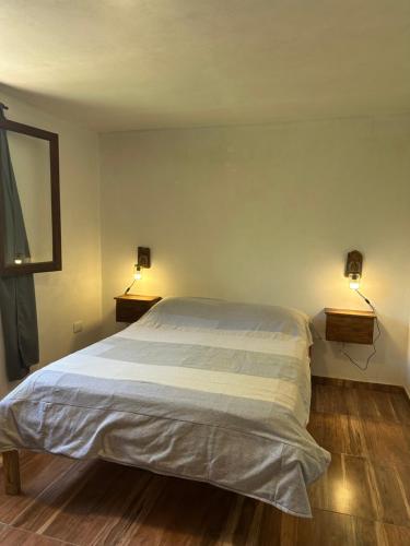 a bedroom with a bed with two lights on the wall at Cabaña El Quebrachal in Valle Hermoso