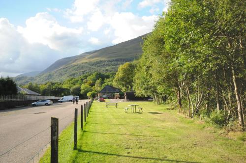 a fence next to a road with a mountain at Blackwater Glamping Pods in Kinlochleven