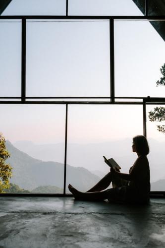 a woman sitting in front of a window reading a book at Scenic Mountain Cabin with Workspace - Close to Ella in Badulla
