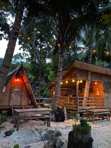 una cabaña con dos bancos y dos palmeras en Alfonsa Tent Ground - Camp By The Sea, en Oslob