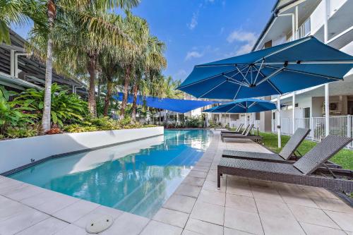 a pool with chairs and an umbrella next to a building at By The Sea Shore With Pool in Airlie Beach