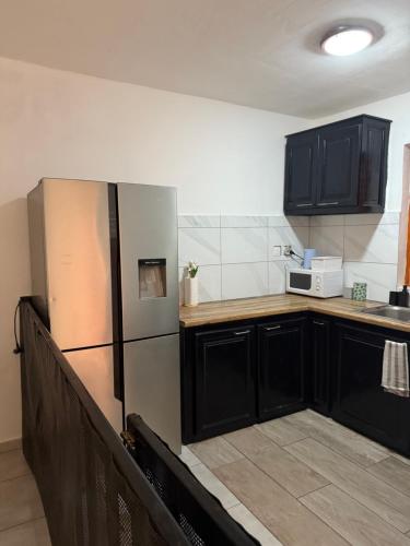 Una cocina con gabinetes negros y un refrigerador de acero inoxidable. en Charmant appartement, en Kani Keli