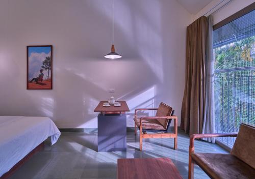 Achutham Cottages Wayanad by VOYE HOMES - Nature Luxe near Banasura Dam في Padinjarathara: غرفة نوم بها سرير وطاولة وكرسي