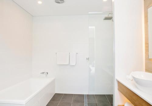 a white bathroom with a shower and a sink at The Esplanade Motel in Batemans Bay