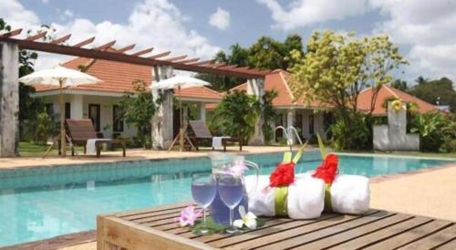 une table avec deux verres à vin et une piscine dans l'établissement Baan Chuengkao Resort, à Ranong