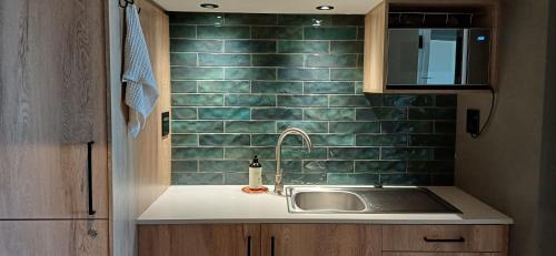 a kitchen with a sink and a green tiled wall at Mitford Marula in Morganʼs Bay