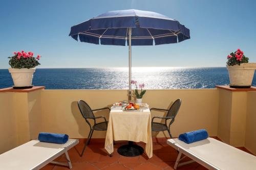 einen Tisch und Stühle mit einem Sonnenschirm und dem Meer in der Unterkunft Hotel Weber Ambassador in Capri