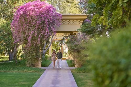 a man and woman walking down a walkway with purple flowers at Grand Hyatt Doha Hotel & Villas in Doha