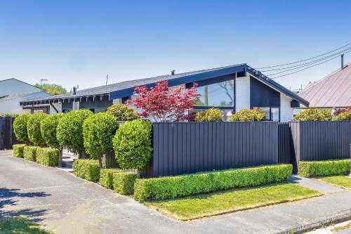 a fence with hedges in front of a house at Modern Two-Bedroom Home in Merivale in Christchurch
