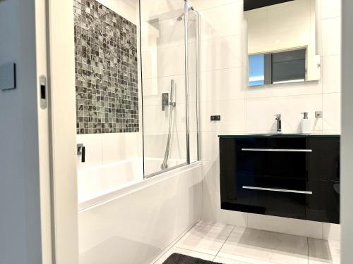 a white bathroom with a shower and a sink at Jacuzzi & Parking Piernikowy Spa Apartment by Rentoom in Toruń