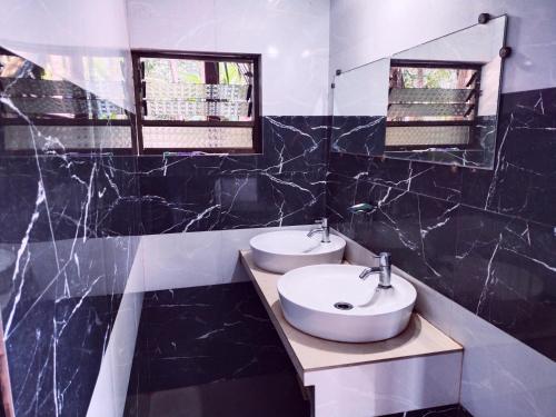 une salle de bain noire et blanche avec deux lavabos et un miroir dans l'établissement Samant Beach Resort, à Malvan