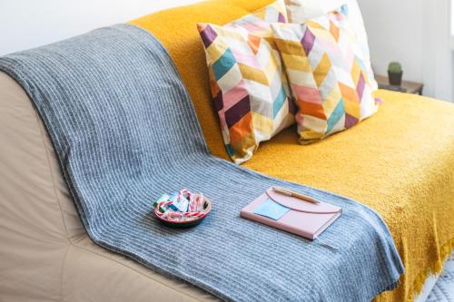 a blanket and a book on a couch with pillows at The cozy corner of Amelie in Nice
