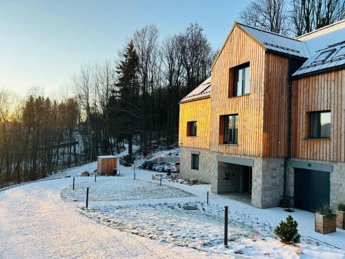 a large wooden house in the snow with a driveway at Apartmány Hraničná s privátním wellness in Bedřichov