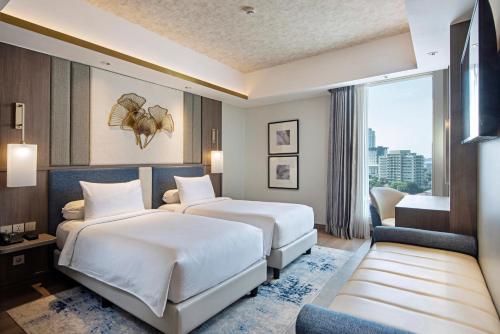 two beds in a hotel room with a window at HARRIS Hotel & Conventions Gubeng in Surabaya