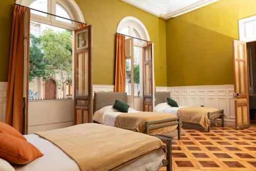 2 Betten in einem Zimmer mit gelben Wänden und Fenstern in der Unterkunft Happy House Hostel in Santiago