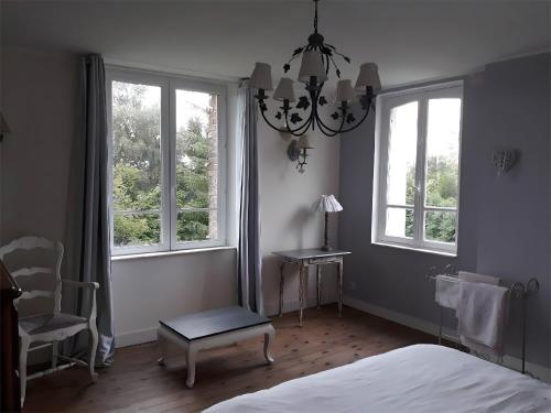 a bedroom with a bed and a chandelier and two windows at Chambres à la campagne La Tuilerie in Prêtreville