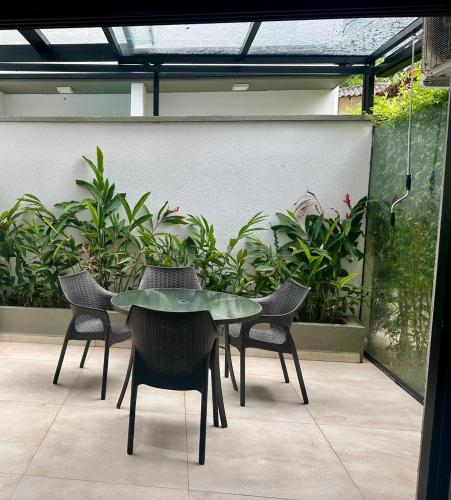 a glass table and chairs on a patio with plants at Casa Nova em Maresias in São Sebastião