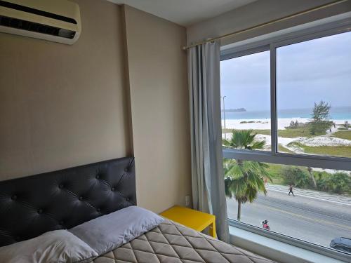 Schlafzimmer mit einem Bett und einem Fenster mit Blick auf den Strand in der Unterkunft PRAIA DO FORTE - PÉ NA AREIA - 6 hóspedes in Cabo Frio