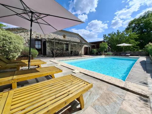 a swimming pool with two wooden benches and an umbrella at Gîte des Gravets in Sigalens