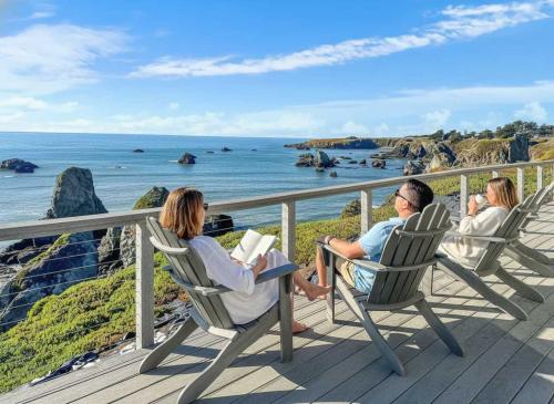 three people sitting in chairs on a deck looking at the ocean at Seaside Elegance Oceanfront Escape with 3 Suites in Bodega Bay