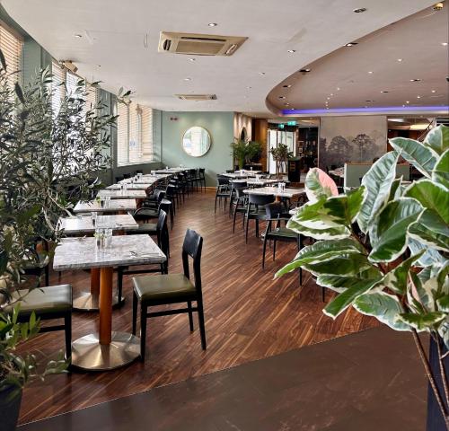 a restaurant with tables and chairs and plants at Best Western London Heathrow Ariel T2 ,3 ,4 in Hillingdon