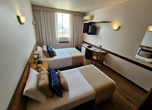a hotel room with two beds and a desk at Hotel Santoni in Guarapuava