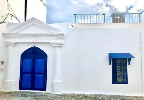 ein weißes Gebäude mit einer blauen Tür und einem Fenster in der Unterkunft la terrasse aux souvenirs in Karthago