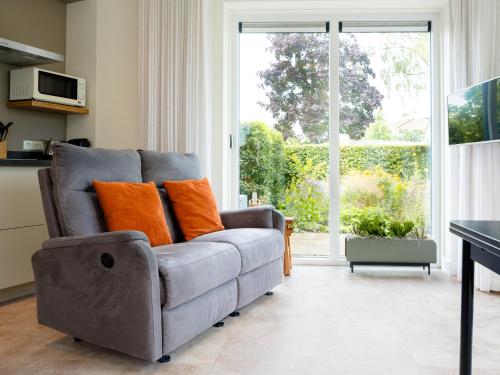 un canapé gris avec des coussins orange dans un salon dans l'établissement Sfeervolle Studio - Privéterras & Vloerverkoeling - Achterhoek, à Almen
