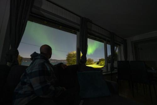 a man sitting in a dark room looking out the window at a aurora at Northern Lights Apartment in Mortenhals