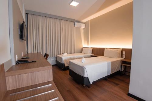 a hotel room with two beds and a desk at Hotel Évora by Rede Sagres in Florianópolis