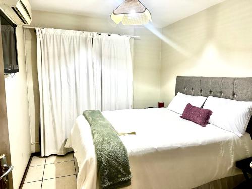 una camera da letto con un letto bianco e una finestra di Feel At Home Cosy Apartment a Gaborone