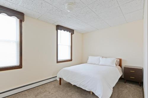 a white bedroom with a bed and two windows at Classic American-style, 18 min to NYC in Carlstadt