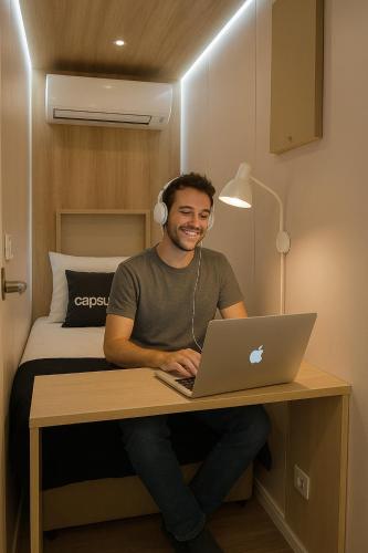 a man sitting at a desk with a laptop and headphones at Capsula Hotel Sao Paulo - Paulista in São Paulo