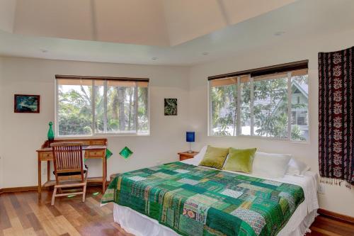 a bedroom with a bed and a desk and two windows at Balinese Beach House With Pool in Pahoa