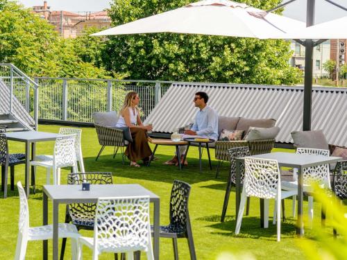ein Mann und eine Frau sitzen an einem Tisch unter einem Sonnenschirm in der Unterkunft Novotel Parma Centro in Parma
