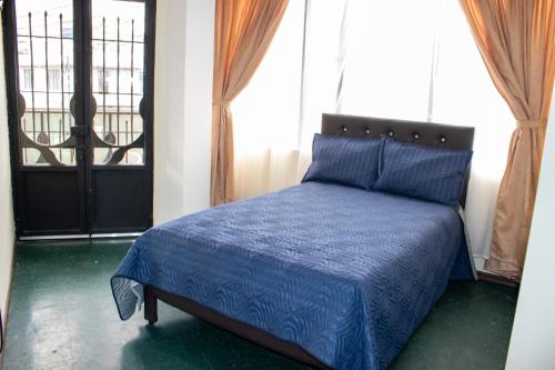 a bedroom with a bed with a blue comforter and a window at Hotel Inti Raymi in Pasto