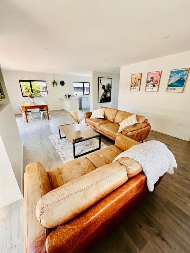 uma sala de estar com dois sofás castanhos e uma mesa em Modern Costal Escape-with Spa em Papamoa