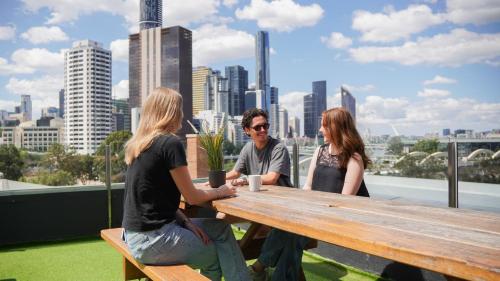 a group of people sitting at a wooden table with a city skyline at Summer House Brisbane in Brisbane