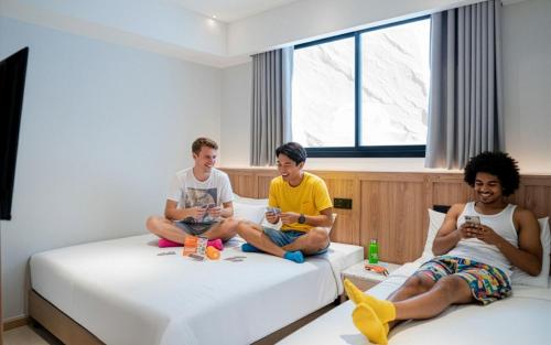 three men sitting on beds looking at their cell phones at Lub d Bangkok Siam - New Look, Across from MBK & Skytrain Access in Bangkok