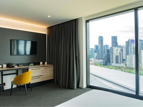 a hotel room with a desk and a large window at Novotel Melbourne South Wharf in Melbourne