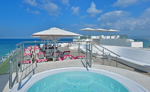 a swimming pool with chairs and umbrellas and the ocean at Hotel Hispania in Playa de Palma