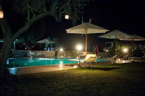 a swimming pool at night with umbrellas and chairs at Dimora del Sole in Putignano
