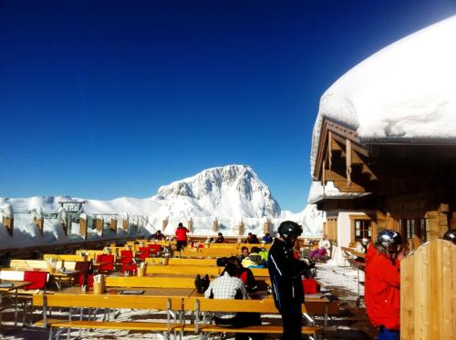 a group of people sitting on benches in front of a mountain at Appartements Nassfeld LUX in Sonnenalpe Nassfeld